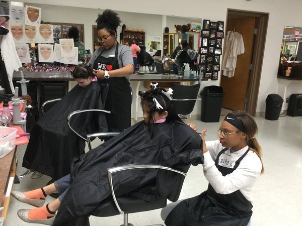 Group of cosmetology students cutting hair at elementary school in salon