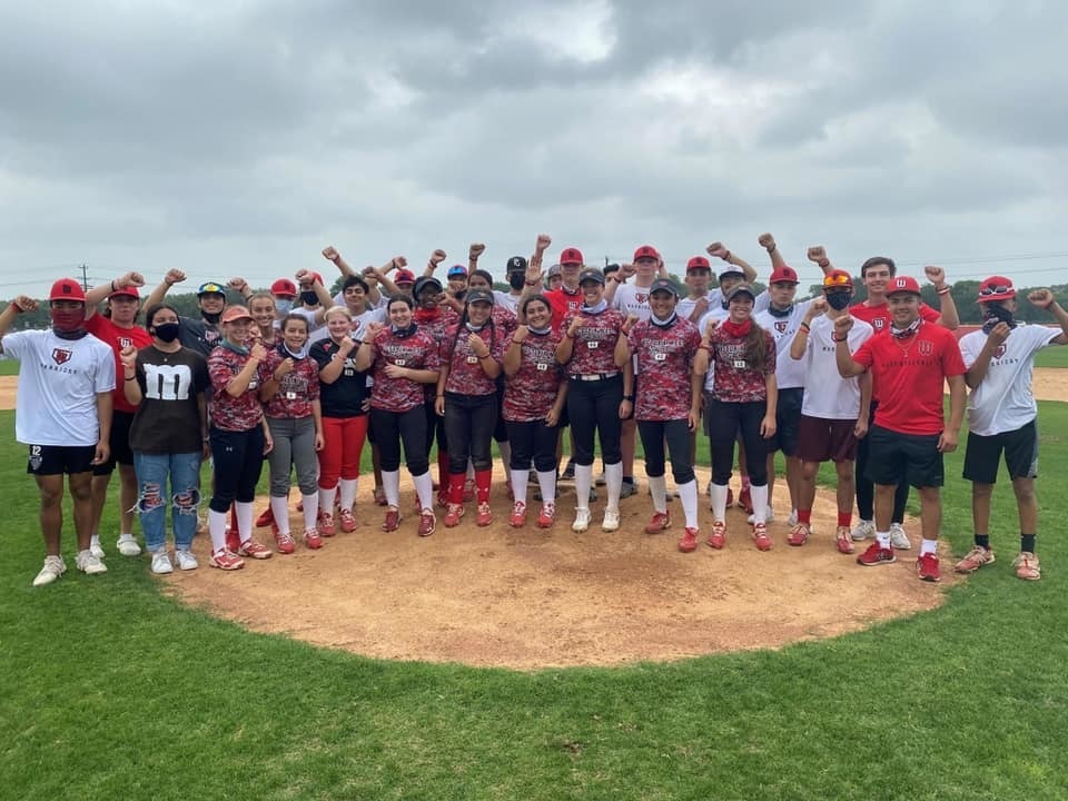 Softball and baseball players stand on mound with fists in air in celebration