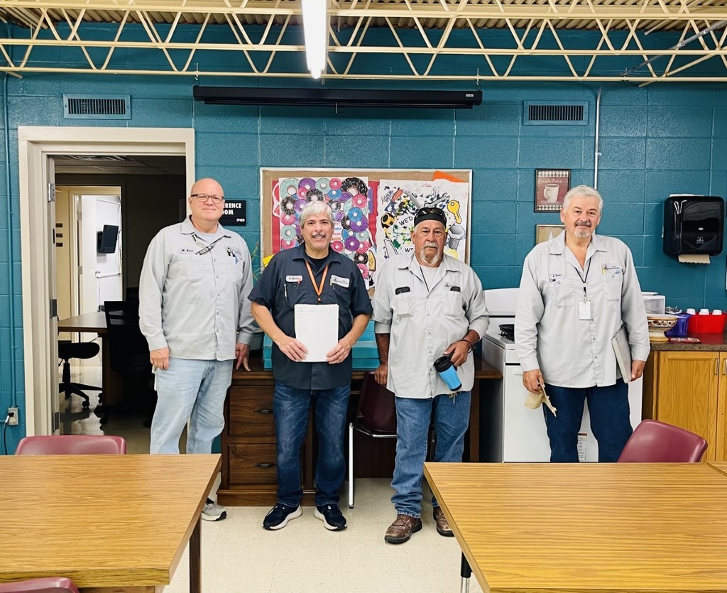 Four maintenance workers standing in front of West's appreciation posters